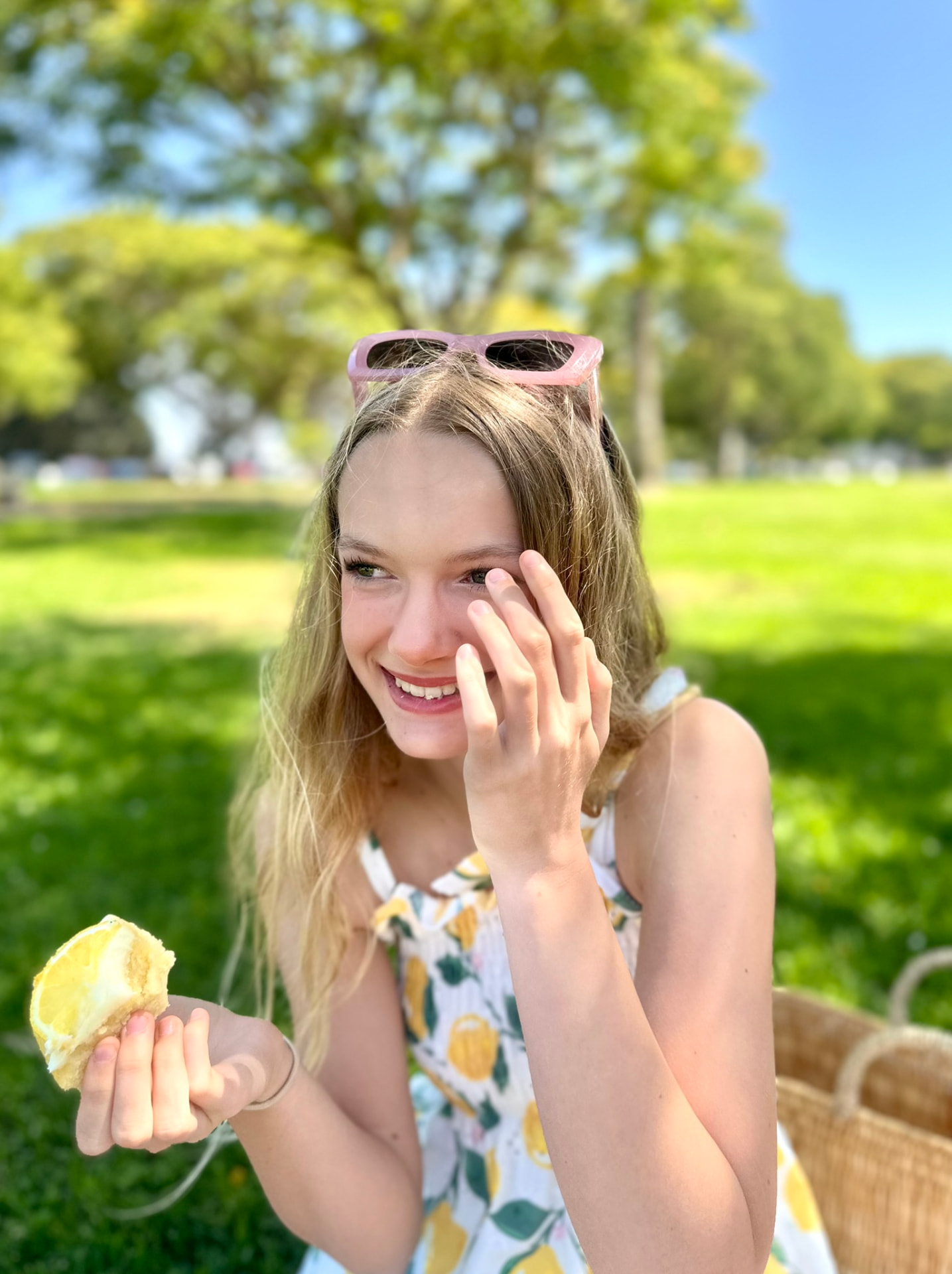 A smiling girl in a lemon-print dress holding a piece of lemon cake in the park
