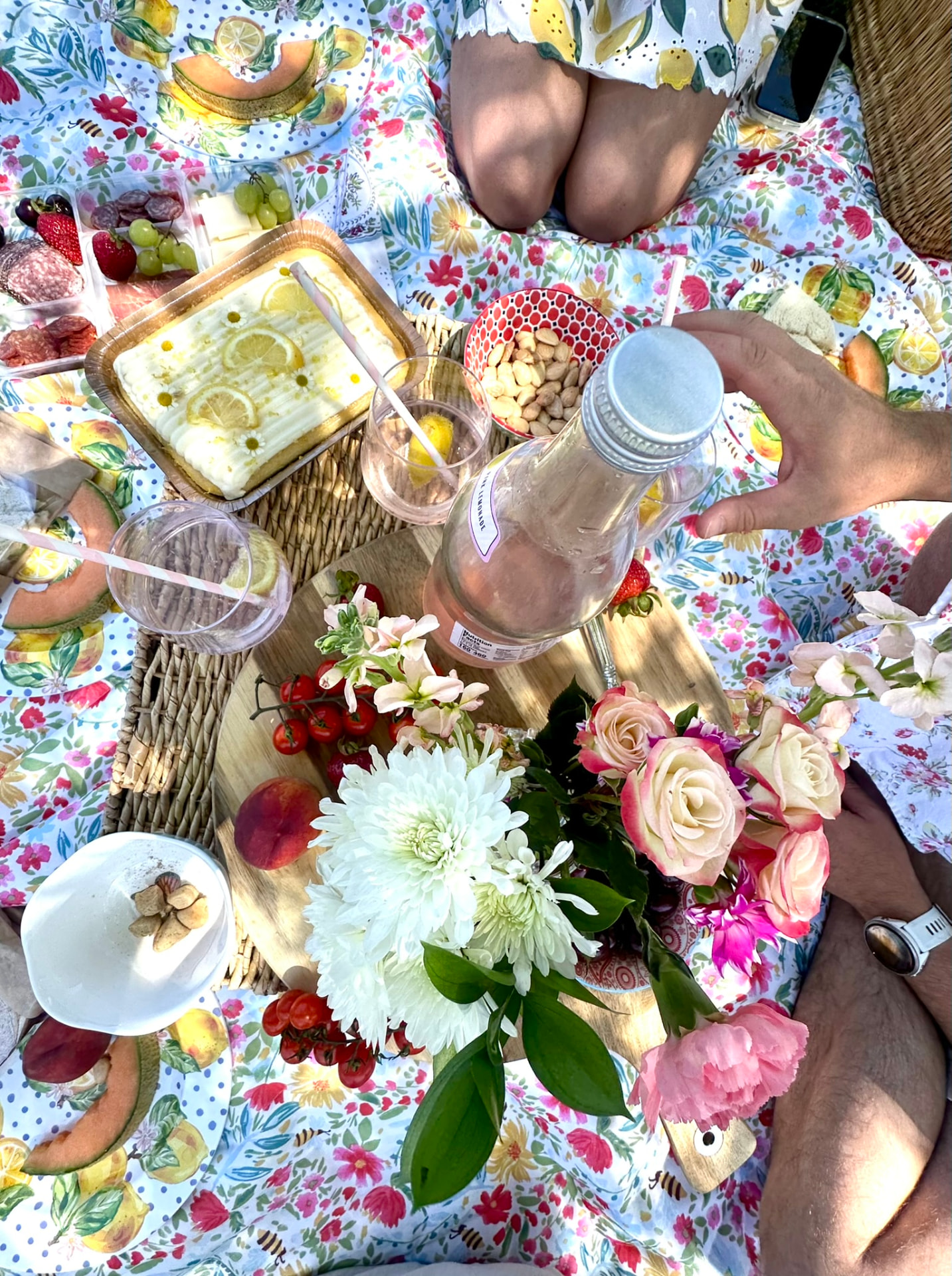 Overhead view of the picnic: lemon cake, fruit, almonds, pink lemonade and a bouquet of roses and mums