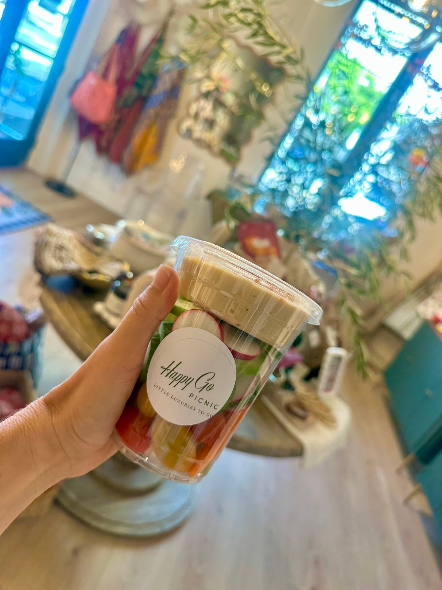 A Happy Go Picnic crudité and hummus cup held up in the shop